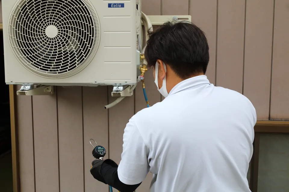 エアコン室外機の配管に計測器をつないで確認する技術者