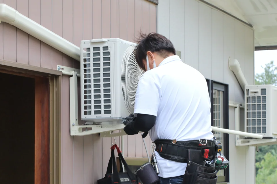 住宅外壁の架台にエアコン室外機を据え付ける技術者