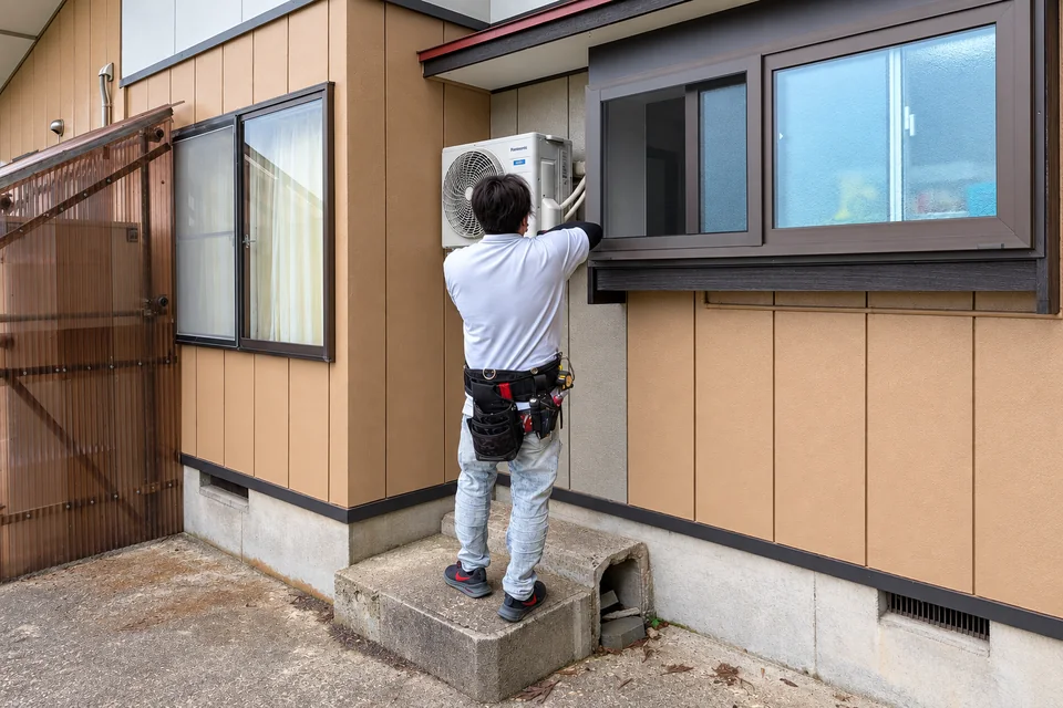 住宅外部でエアコン室外機を施工する技術者